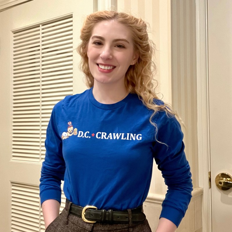 Smiling person wearing a blue 'D.C. Crawling' shirt, standing indoors.